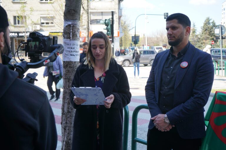 A speaker reading a statement at an outdoor commemoration while a camera crew films